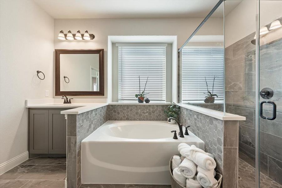 Inviting garden tub and walk in tiled shower. Separate vanities have framed mirrors and bronze fixtures and hardware.