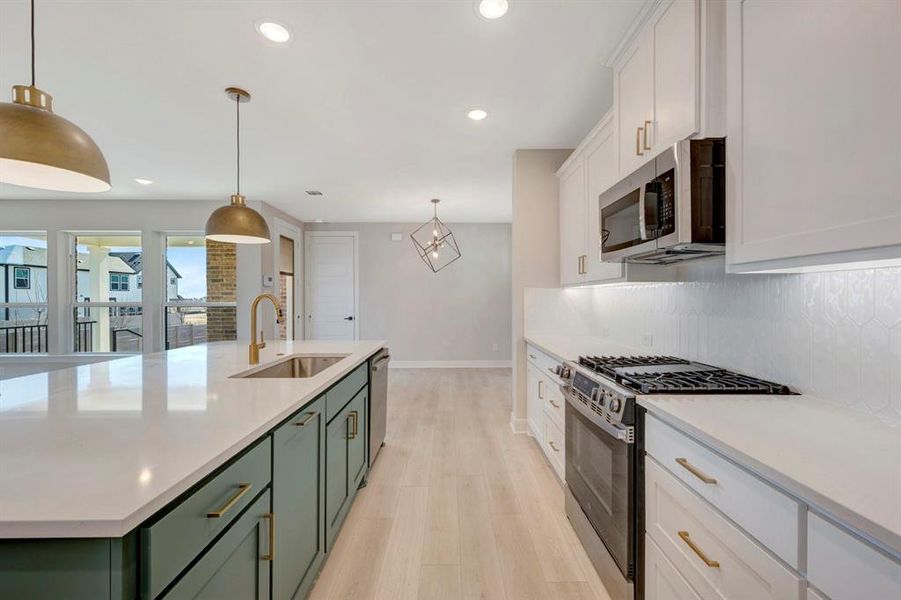 Two tone kitchen featuring dual tone cabinetry, stainless steel appliances, light wood finished floors, an island with sink, and light stone counters