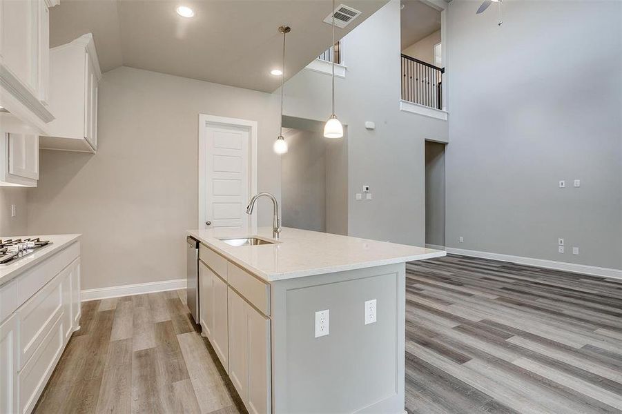 Kitchen with decorative light fixtures, light wood-type flooring, sink, a center island with sink, and a towering ceiling