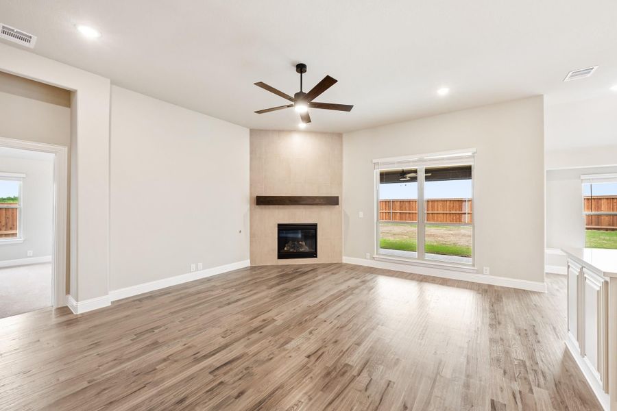 Open living room with hardwood floors, ceiling fan, and corner fireplace with wood mantel Open living room with hardwood floors, ceiling fan, and corner fireplace with wood mantel