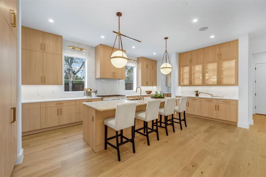 Kitchen with light brown cabinets, a breakfast bar, light stone countertops, decorative light fixtures, and modern cabinets
