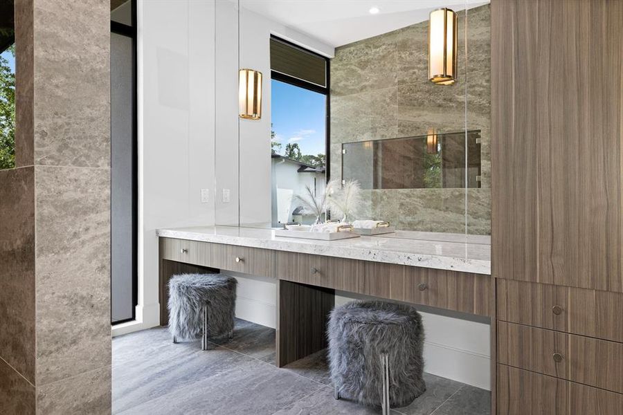 The double vanity area is ideal for morning routines, featuring River White countertops and a makeup vanity with knee space. It is complemented by Heritage Luxe-Matte tile flooring, abundant built-in cabinetry, and sconce lighting, offering both practicality and elegance for getting ready in style.