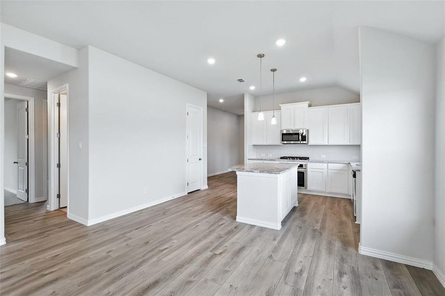 Kitchen with stainless steel microwave, light wood-style floors, a kitchen island, white cabinets, and decorative light fixtures
