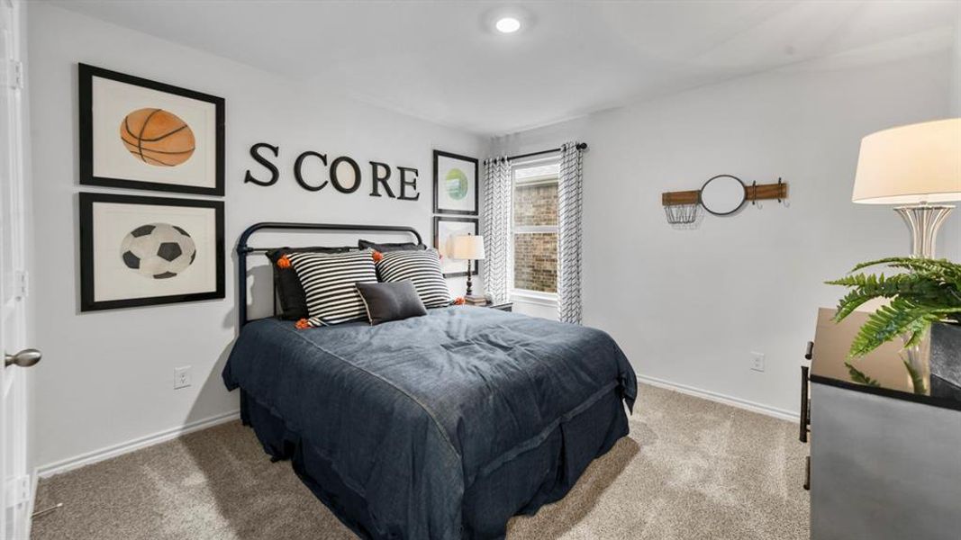 Carpeted room featuring a window with patterned curtains, a black metal bed frame, and crisp white walls Carpeted room featuring a window with patterned curtains, a black metal bed frame, and crisp white walls