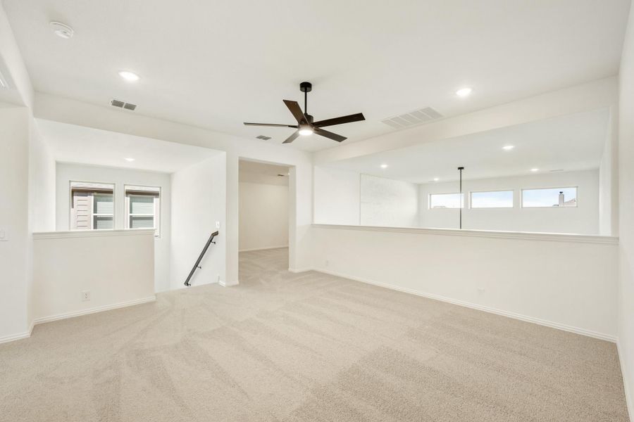 Spacious upstairs loft with beige carpet, ceiling fan, recessed lighting, and open staircase railing