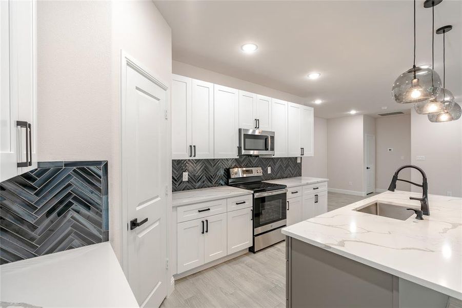 Kitchen with white cabinets, appliances with stainless steel finishes, hanging light fixtures, and sink