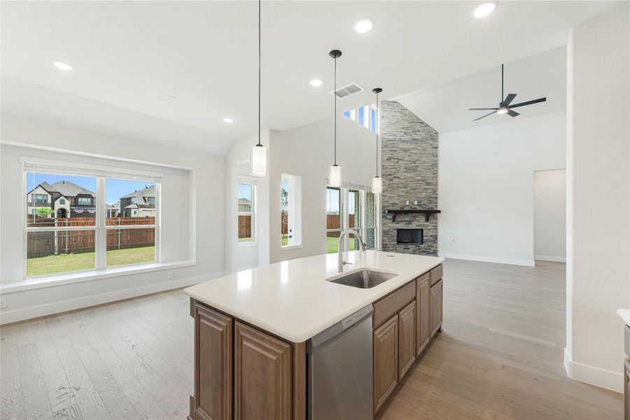 Open-concept kitchen with center island, sink, pendant lights, and stone fireplace in adjoining living area with vaulted ceiling Open-concept kitchen with center island, sink, pendant lights, and stone fireplace in adjoining living area with vaulted ceiling