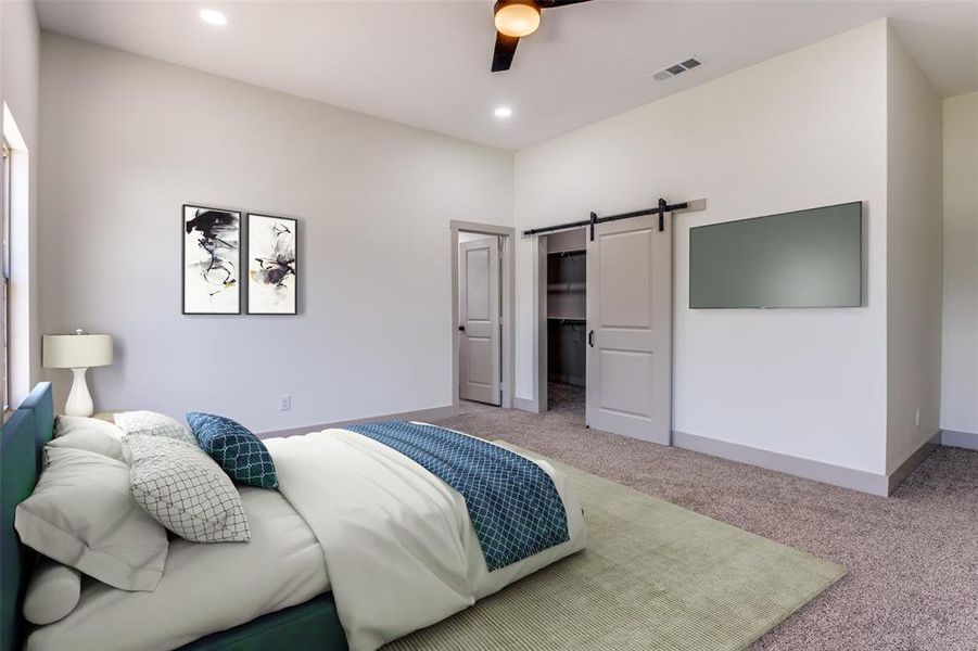 Bedroom featuring ceiling fan, a barn door, a walk in closet, a closet, and carpet