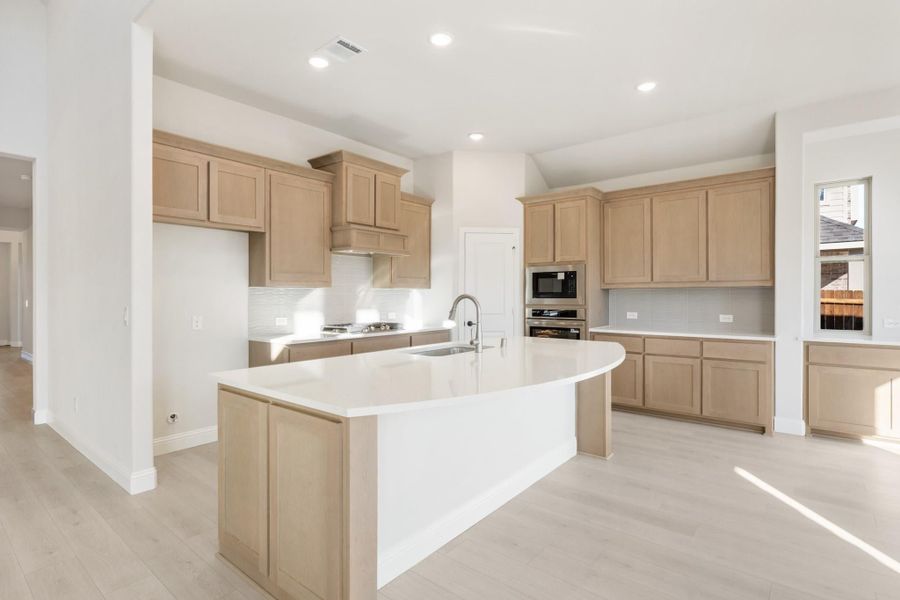 Kitchen with large curved island, tan cabinets, white countertops, and stainless steel appliances
