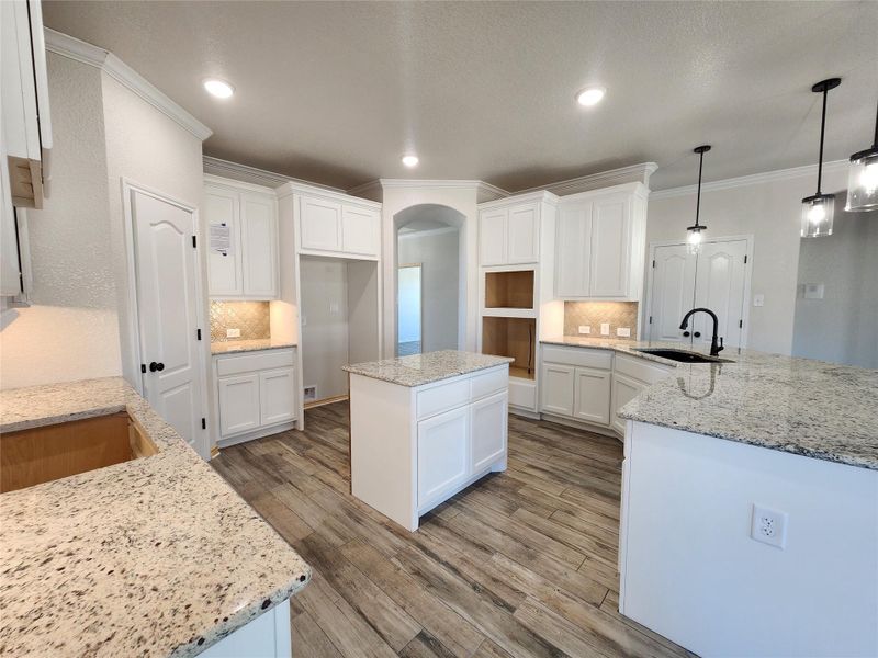 Kitchen with decorative backsplash, wood finished floors, light stone countertops, white cabinets, and recessed lighting
