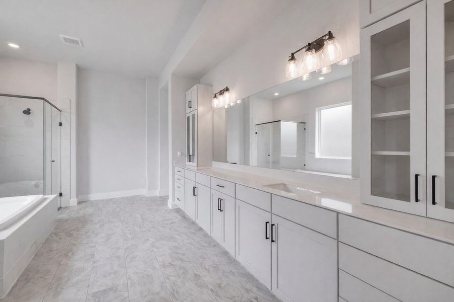 Spacious bathroom featuring white cabinetry with black hardware, a long vanity with dual sinks, a large mirror, and a glass-enclosed shower