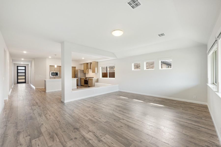 Open-concept living area with light wood floors, white walls, and kitchen visible in background