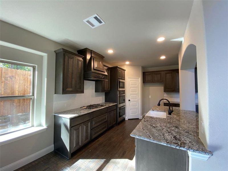 Kitchen with stainless steel appliances, dark wood-type flooring, and a healthy amount of sunlight