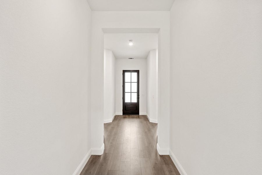 Hallway with white walls, wood floors, and black-framed glass front door at the end