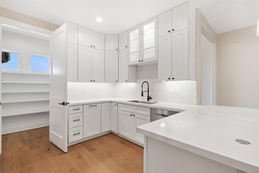 Kitchen with white cabinets, backsplash, light wood-style floors, and a sink Kitchen with white cabinets, backsplash, light wood-style floors, and a sink