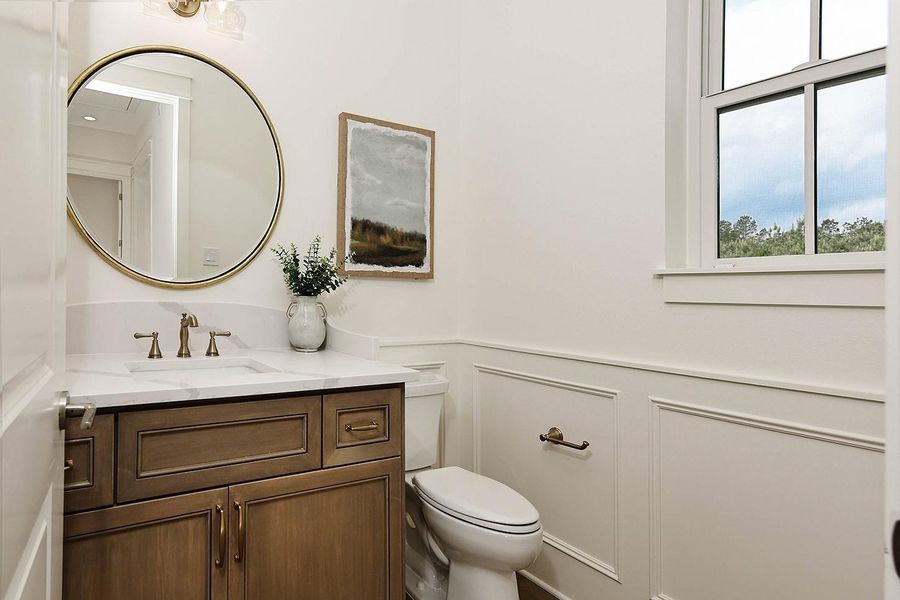 Powder bath is elegant with custom wainscoting, rich wood stained vanity with storage, quartz counter and antique gold/bronze fixtures.