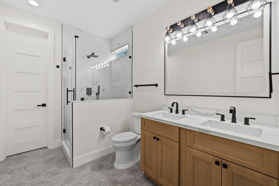 Modern bathroom featuring a sleek double vanity with black fixtures, a spacious glass-enclosed shower, and elegant hexagonal tile flooring for a stylish touch.