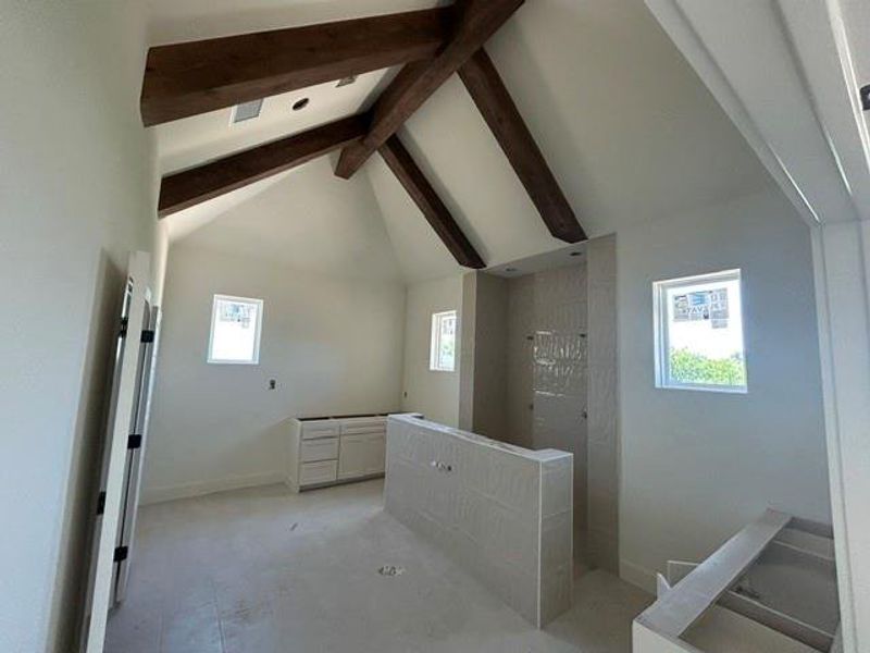 Vaulted ceiling featuring exposed wood beams, multiple windows, a tiled shower enclosure, and a vanity cabinet base