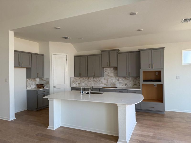 Kitchen with gray cabinets, light stone counters, a center island with sink, and light wood-style flooring Kitchen with gray cabinets, light stone counters, a center island with sink, and light wood-style flooring