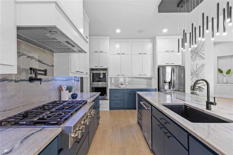Kitchen with tasteful backsplash, light stone counters, white cabinetry, appliances with stainless steel finishes, and blue cabinetry
