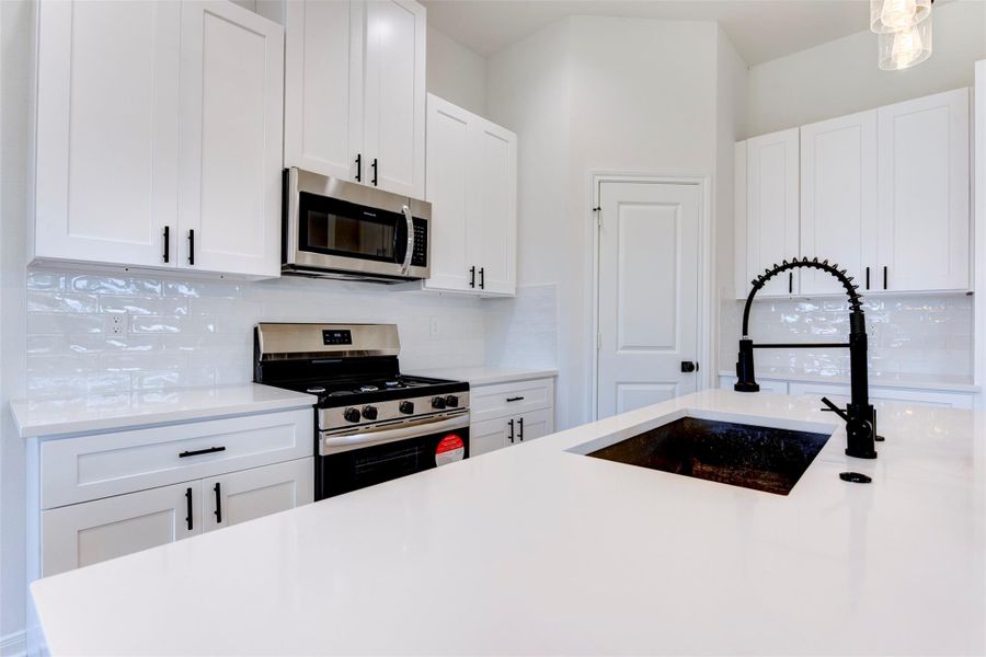 Crisp kitchen design with quartz countertops, shaker cabinetry, and a glossy subway tile backsplash. Matte black fixtures and hardware add contrast, while stainless appliances and a spacious pantry keep the space both stylish and functional.