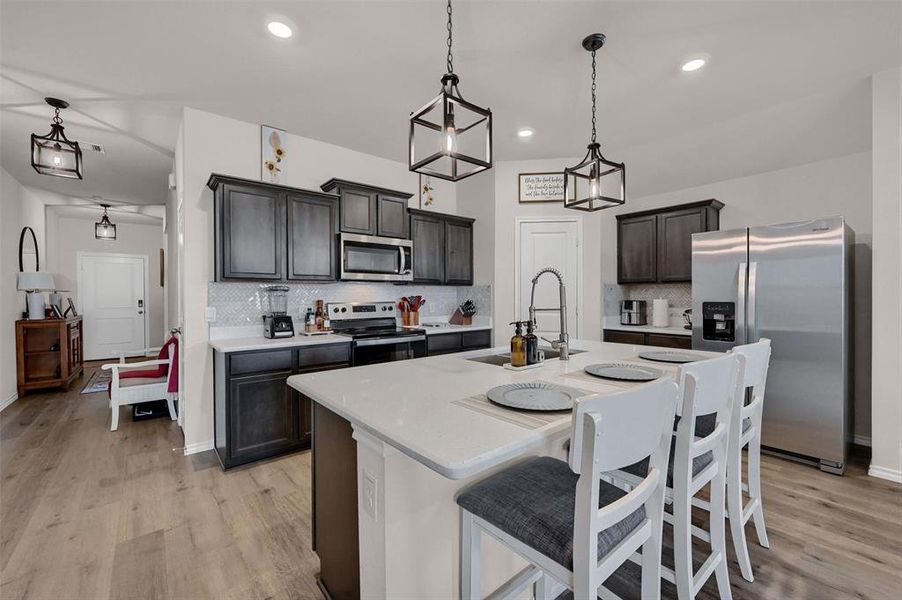 Kitchen featuring light countertops, light wood finished floors, appliances with stainless steel finishes, hanging light fixtures, and a kitchen breakfast bar
