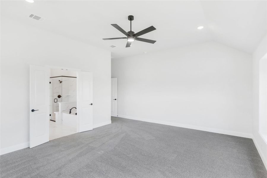 Spacious bedroom with gray carpet, ceiling fan, and open ensuite bathroom with tub and shower visible. Spacious bedroom with gray carpet, ceiling fan, and open ensuite bathroom with tub and shower visible.