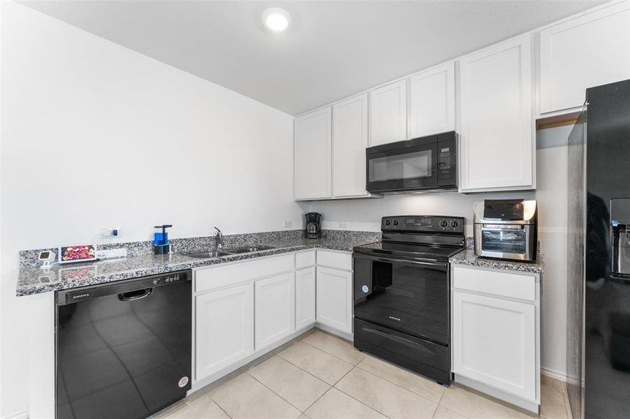 Kitchen with black appliances, white cabinets, dark stone countertops, and light tile patterned floors Kitchen with black appliances, white cabinets, dark stone countertops, and light tile patterned floors