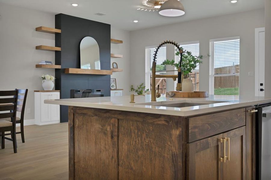 Kitchen featuring open shelves, light wood-style floors, light countertops, a sink, and a glass covered fireplace Kitchen featuring open shelves, light wood-style floors, light countertops, a sink, and a glass covered fireplace