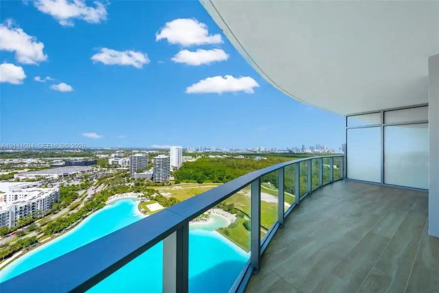 Curved balcony featuring wood-finish tile flooring, glass railings, and expansive architectural overhang Curved balcony featuring wood-finish tile flooring, glass railings, and expansive architectural overhang