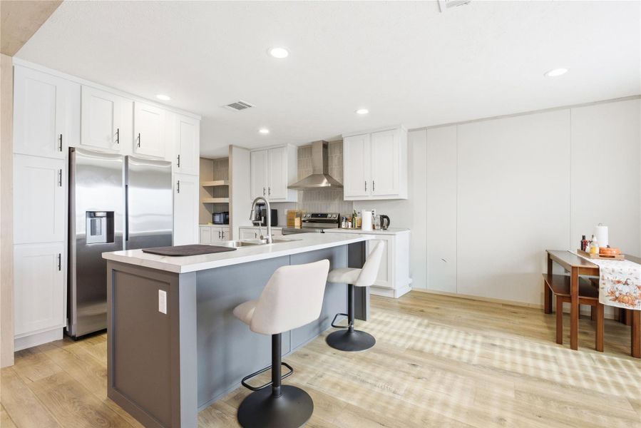 A contemporary kitchen features bright white cabinetry, stainless steel appliances, and an inviting island with a breakfast bar.