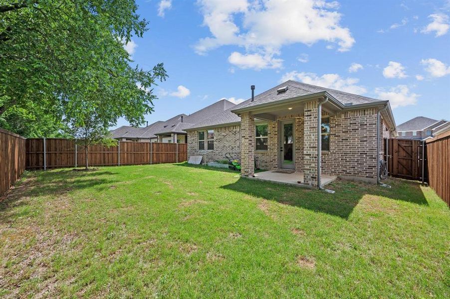 Private backyard featuring a covered patio, extensive lawn, full perimeter wood fencing, and a side gate entry Private backyard featuring a covered patio, extensive lawn, full perimeter wood fencing, and a side gate entry