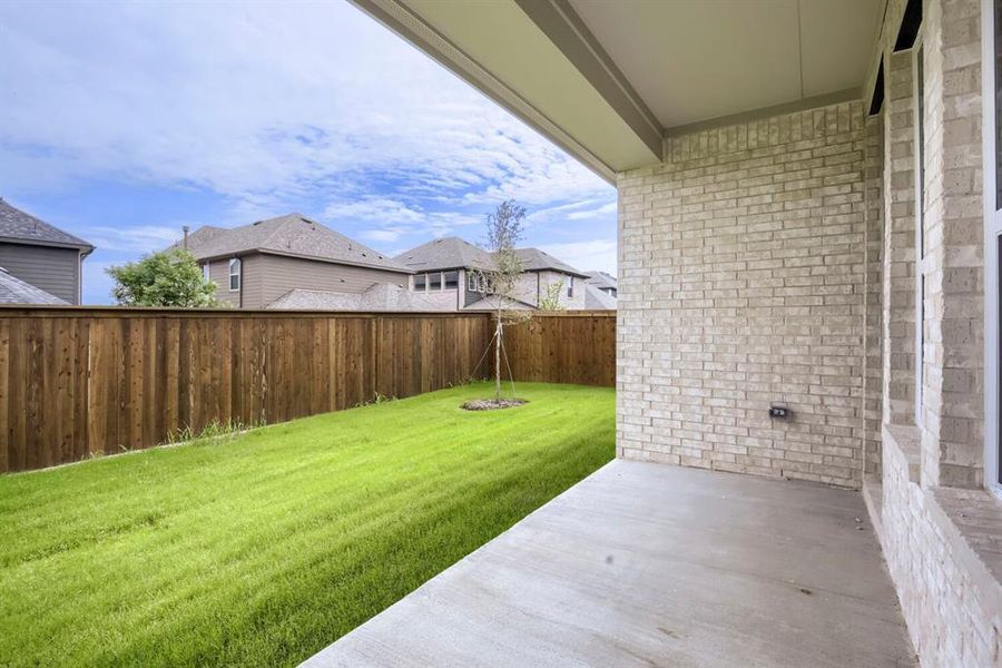 Covered outdoor patio with a concrete surface, light-colored brick exterior, and a spacious green lawn