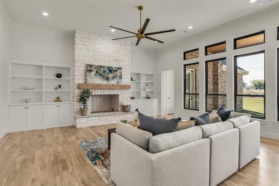 Living room with recessed lighting, ceiling fan, a stone fireplace, light wood finished floors, and crown molding Living room with recessed lighting, ceiling fan, a stone fireplace, light wood finished floors, and crown molding