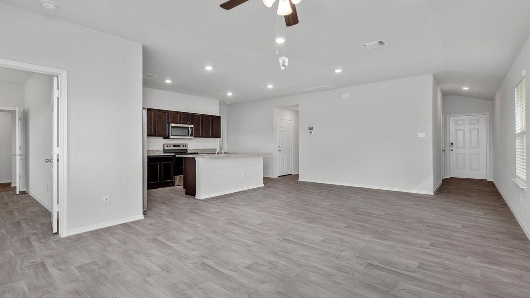 Kitchen with open floor plan, a ceiling fan, dark wood finish cabinets, a center island with sink, and stainless steel appliances