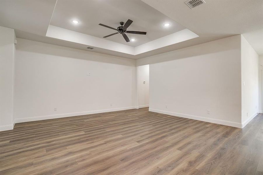 Empty room with a tray ceiling, wood finished floors, ceiling fan, and recessed lighting