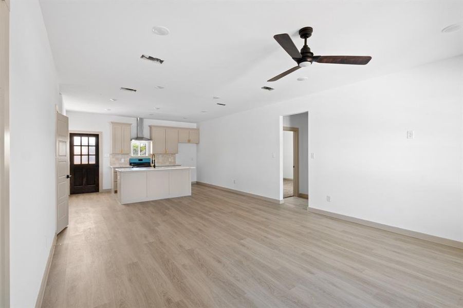 Unfurnished living room with light wood-type flooring, visible vents, baseboards, and ceiling fan Unfurnished living room with light wood-type flooring, visible vents, baseboards, and ceiling fan