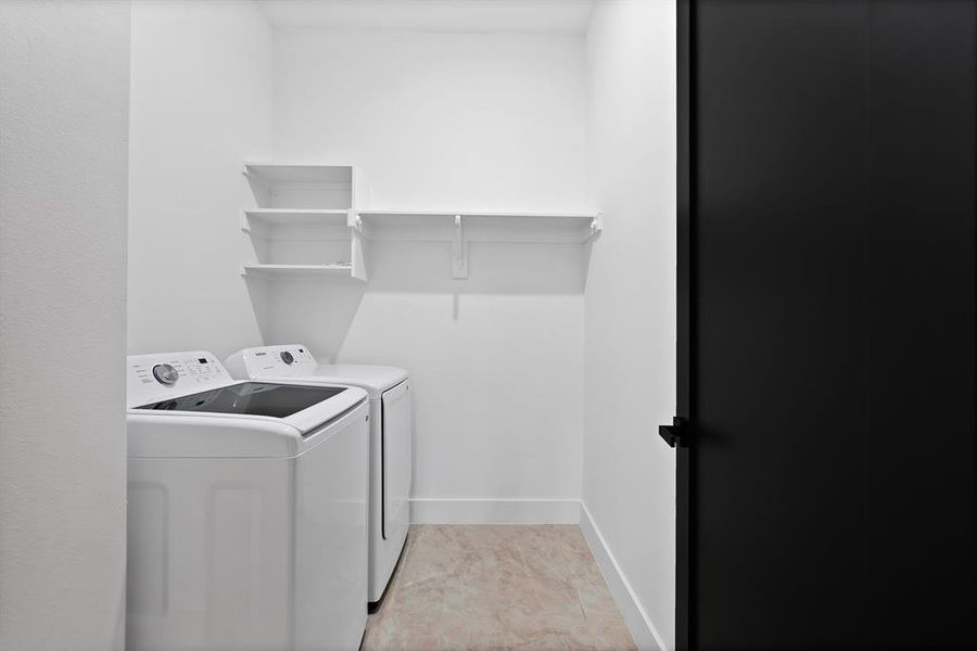 Utility space featuring a washer and dryer, wall-mounted shelving, and tiled flooring