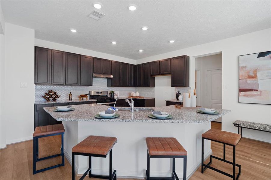 This kitchen will not disappoint! Your family and guests will enjoy many nights of fun, food and entertainment with ample counter space and kitchen island for setting up a wonderful array of provisions! This view of this gorgeous kitchen showcases SS appliances, granite countertops, beautiful tile backsplash, gas range, high ceiling, recessed lighting and vinyl plank floors!