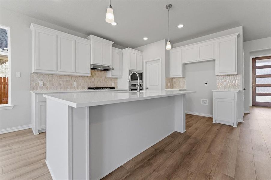 Kitchen featuring white cabinetry, decorative light fixtures, light wood-style floors, a kitchen island with sink, and light stone countertops