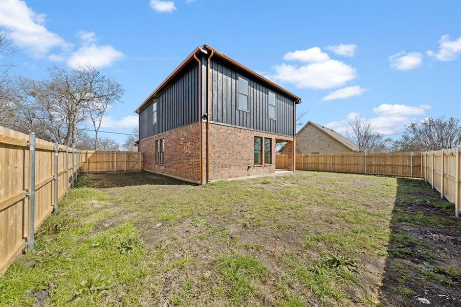 Rear view of house with board and batten siding, a fenced backyard, brick siding, and a lawn