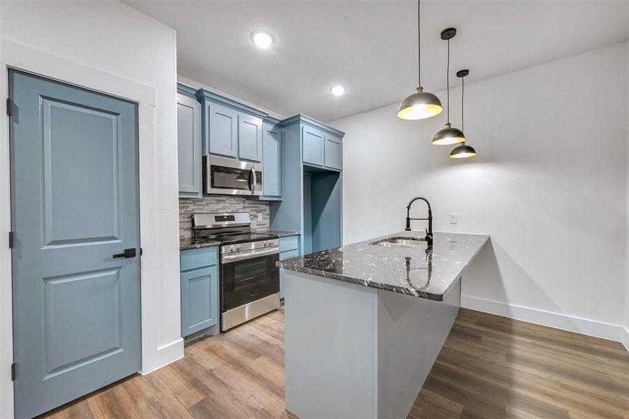 Kitchen with dark stone countertops, a peninsula, light wood-style flooring, appliances with stainless steel finishes, and a sink