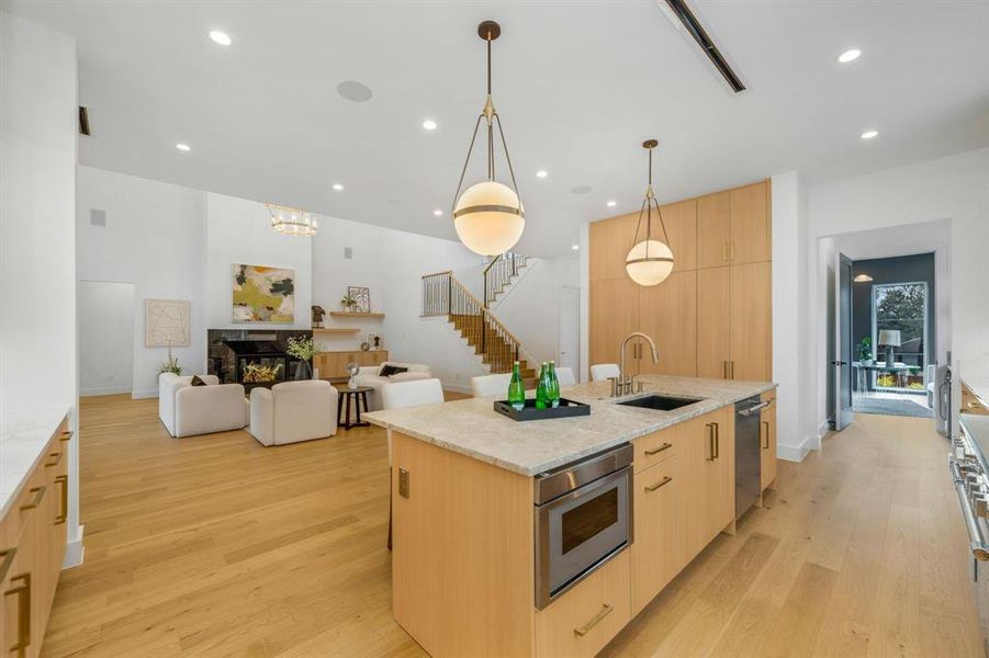 Kitchen featuring light brown cabinets, modern cabinets, a fireplace, light stone counters, and a center island with sink