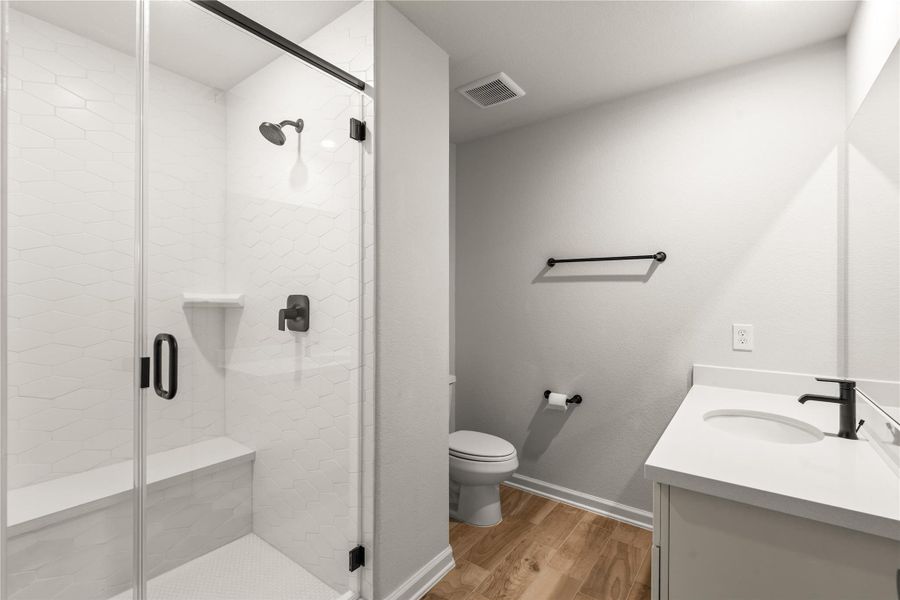 Modern bathroom featuring a sleek glass-enclosed shower with stylish fixtures, a pristine vanity, and elegant wood flooring.