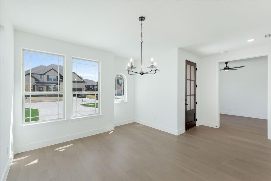 Empty dining room with hardwood floors, chandelier, large windows, and dark wood French door.