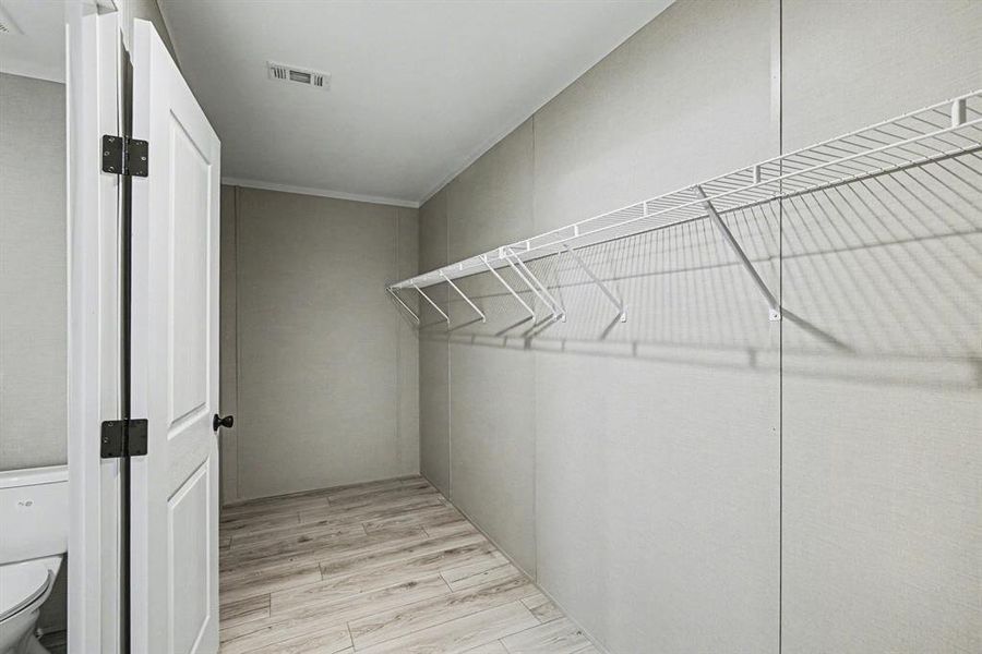 Walk-in closet in primary bathroom featuring light wood-look flooring, white wire shelving, and a white interior door with dark hardware