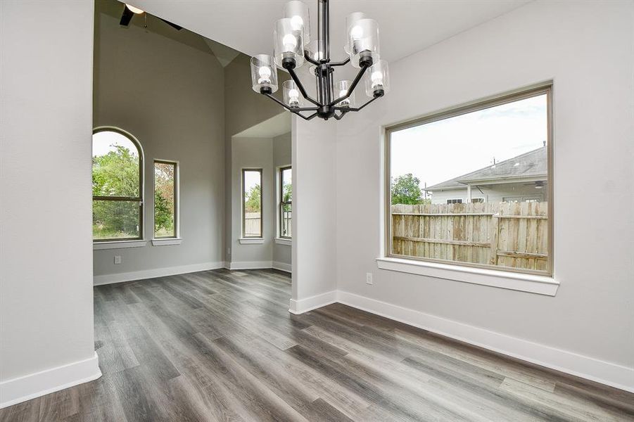 This is spacious dinning room featuring modern gray wood flooring, large windows that let in plenty of natural light, and a stylish black chandelier. The neutral color palette offers a versatile backdrop for your personal decor touches.