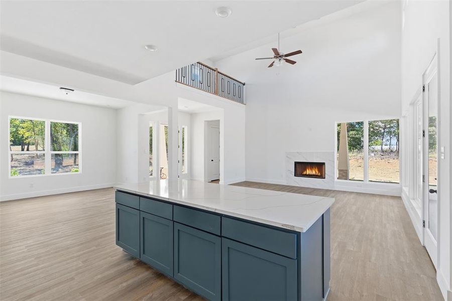 Kitchen with blue cabinetry, open floor plan, a high end fireplace, light wood finished floors, and a high ceiling Kitchen with blue cabinetry, open floor plan, a high end fireplace, light wood finished floors, and a high ceiling