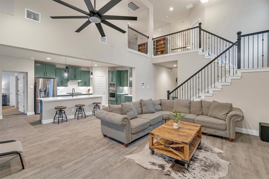 Living room with ceiling fan, light wood-style floors, recessed lighting, and a high ceiling
