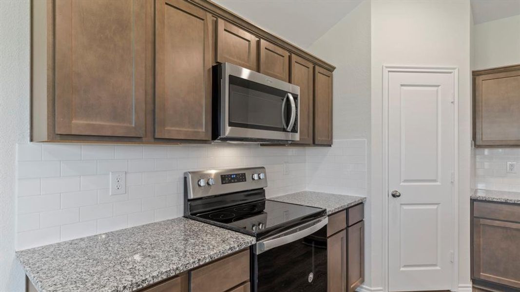 Kitchen featuring dark wood-finish cabinetry, stainless steel appliances, speckled stone countertops, and a white subway tile backsplash